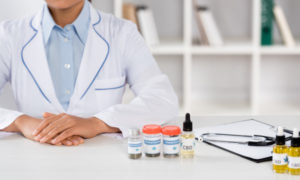 cropped view of african american doctor in white coat near bottles with medical cannabis and cbd